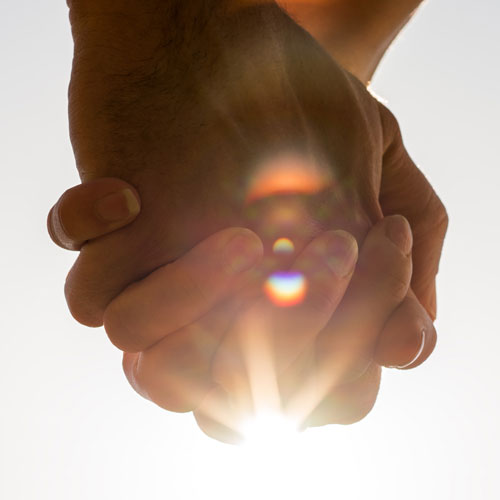 clasped hands with sunshine in the background